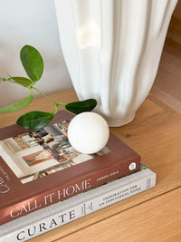 CoTheory Orbit Table Sculpture small white onyx sphere on books with plant and vase background