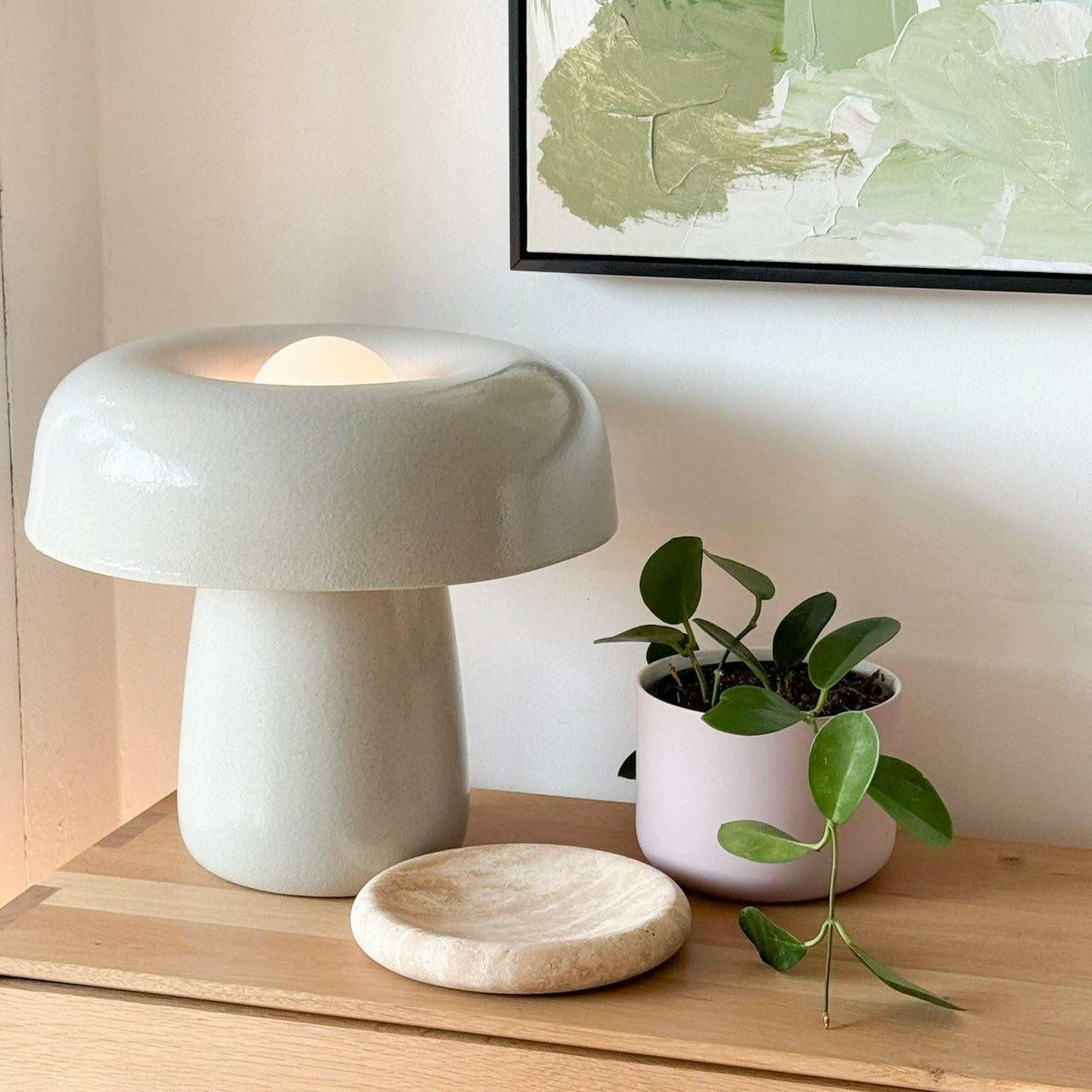 Small beige travertine tray with graceful curves on wooden surface next to modern white lamp and potted plant