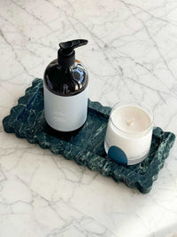 CoTheory Verdi Alpi scalloped marble tray with dark green marble pattern holding a black pump bottle and a white candle on a marble countertop