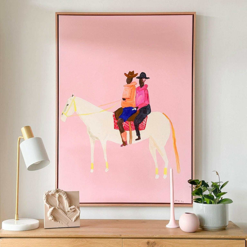 Oak framed Lottie Rae Smooth Operator fine art canvas print with pink background and two figures riding a white horse on a wooden surface with decorative objects