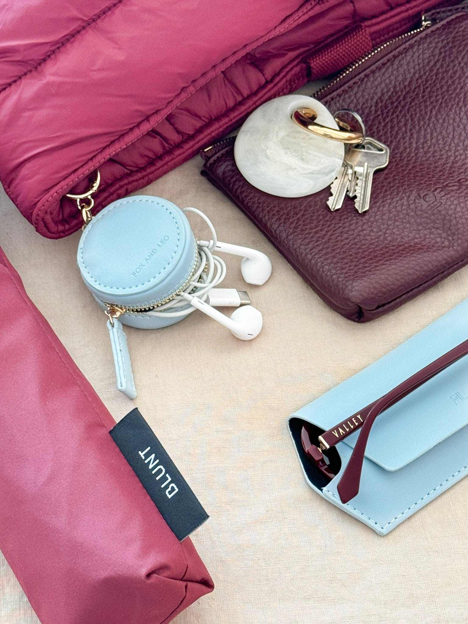 Fox and Leo sky blue leather eye catcher bag charm with microfiber cleaning cloth clipped to a pink bag next to keys and sunglasses case.