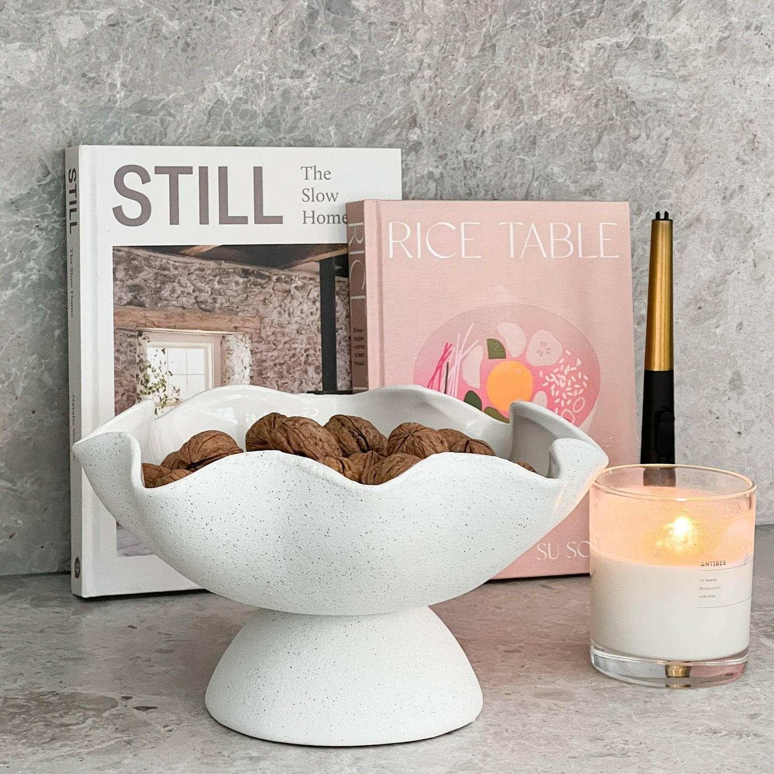 Ripple White Pedestal Bowl ceramic fruit bowl with textured exterior and glossy interior filled with walnuts on a countertop.