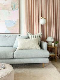 Baya Cyprian Oblong Cushion in oatmeal on a grey sofa with striped pillow and pink curtains in modern living room