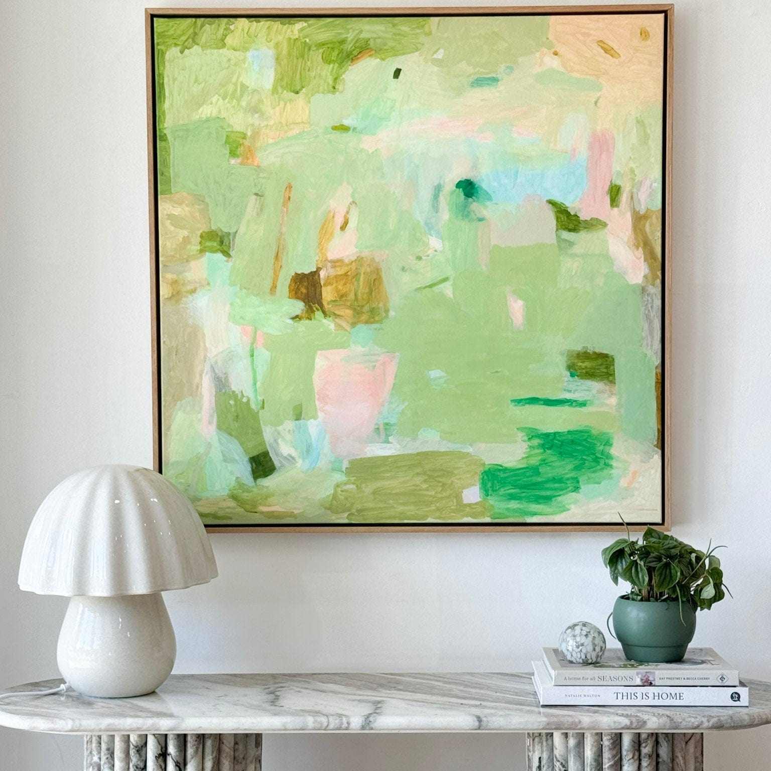 Limited edition abstract art print Lovely Day by Vanni on canvas with soft green and pastel colors in floating oak frame above marble table with lamp and plants