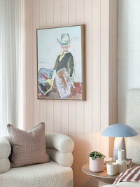Oak framed Marcia Priestley 'Chaps II' limited edition canvas print hanging on pastel pink wall above modern armchair and side table.