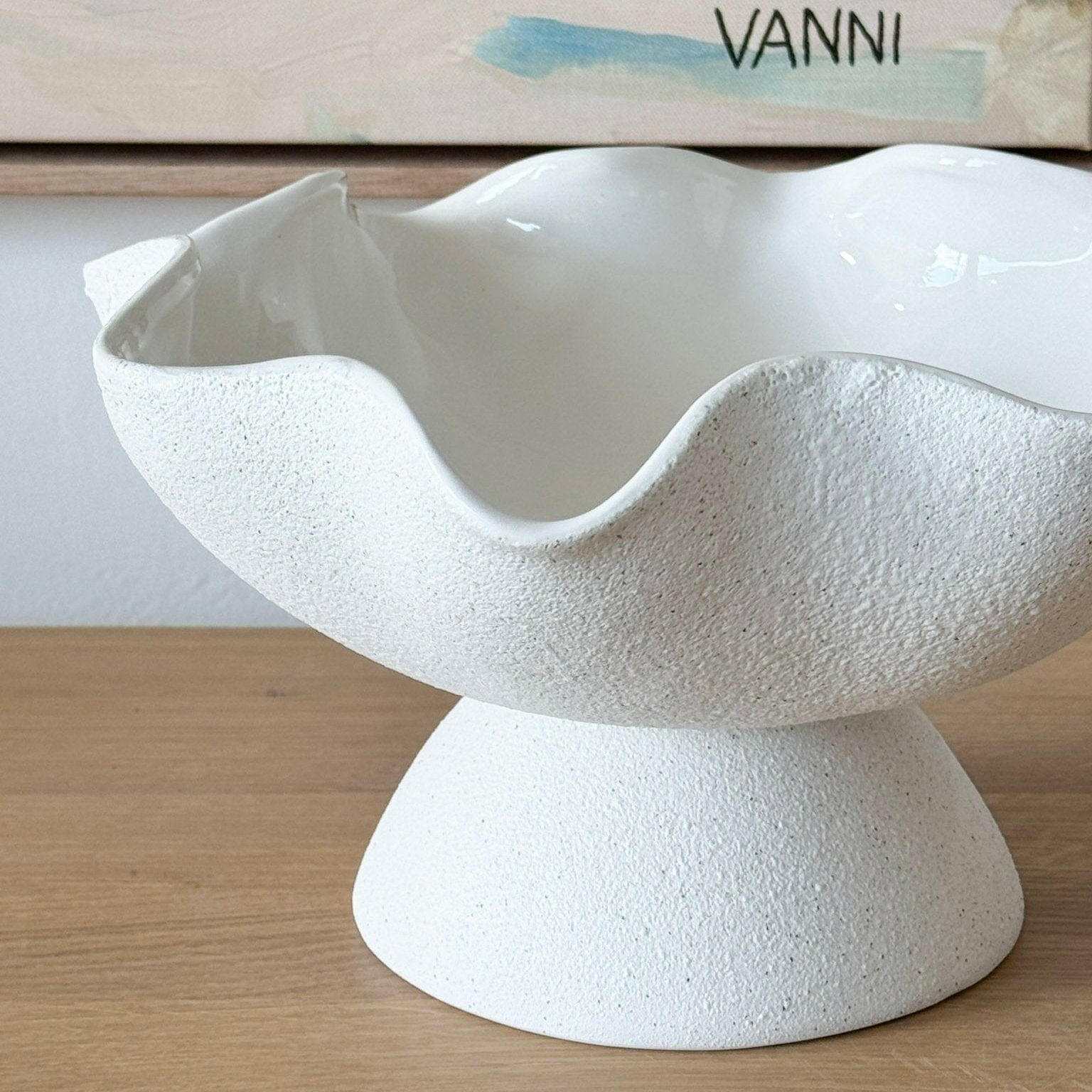 Ripple white ceramic pedestal bowl with glossy interior and textured exterior on wooden surface