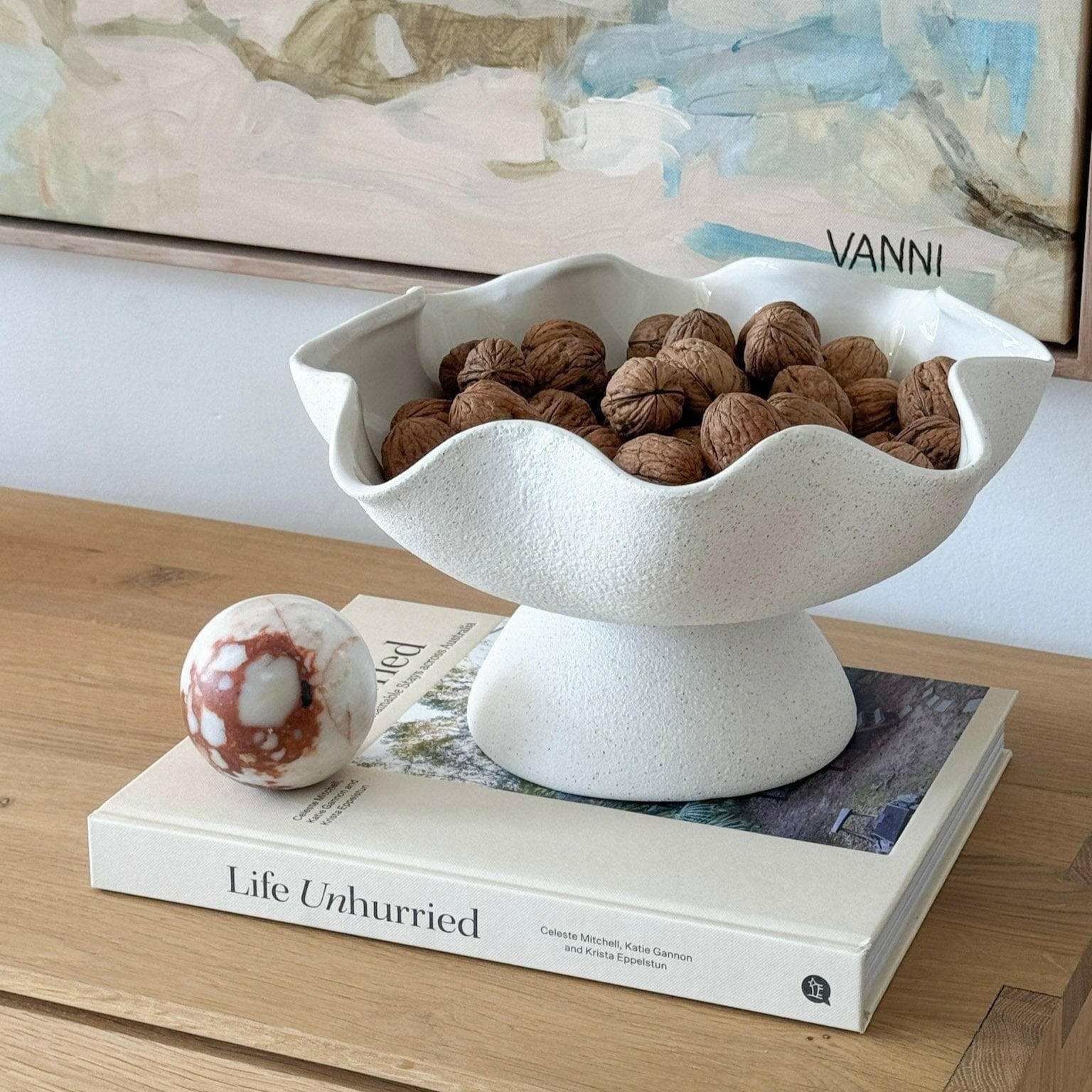 Ripple White Pedestal Bowl ceramic fruit bowl with textured exterior filled with walnuts on a wooden table.