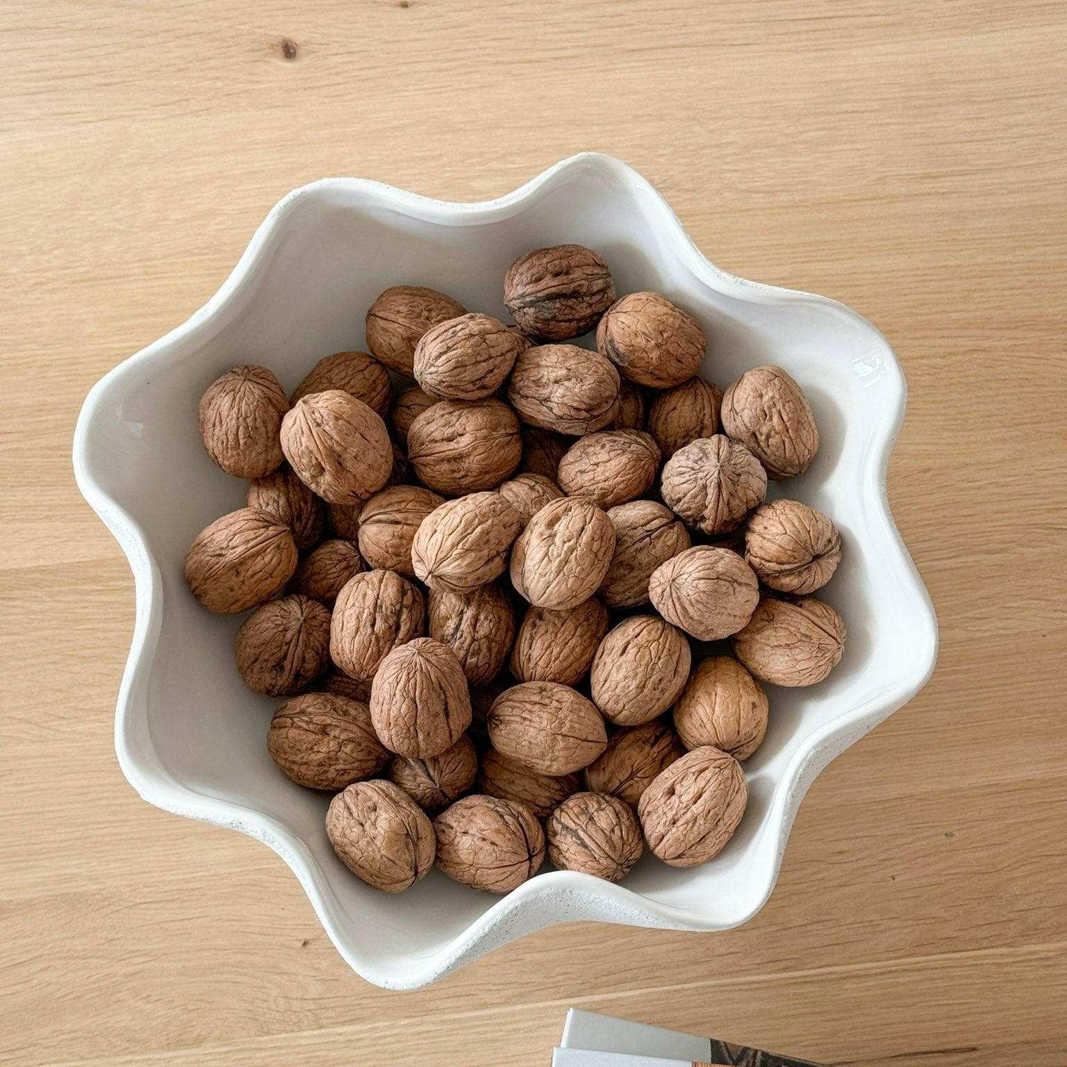 Ripple white ceramic pedestal bowl with textured exterior filled with walnuts on wooden surface
