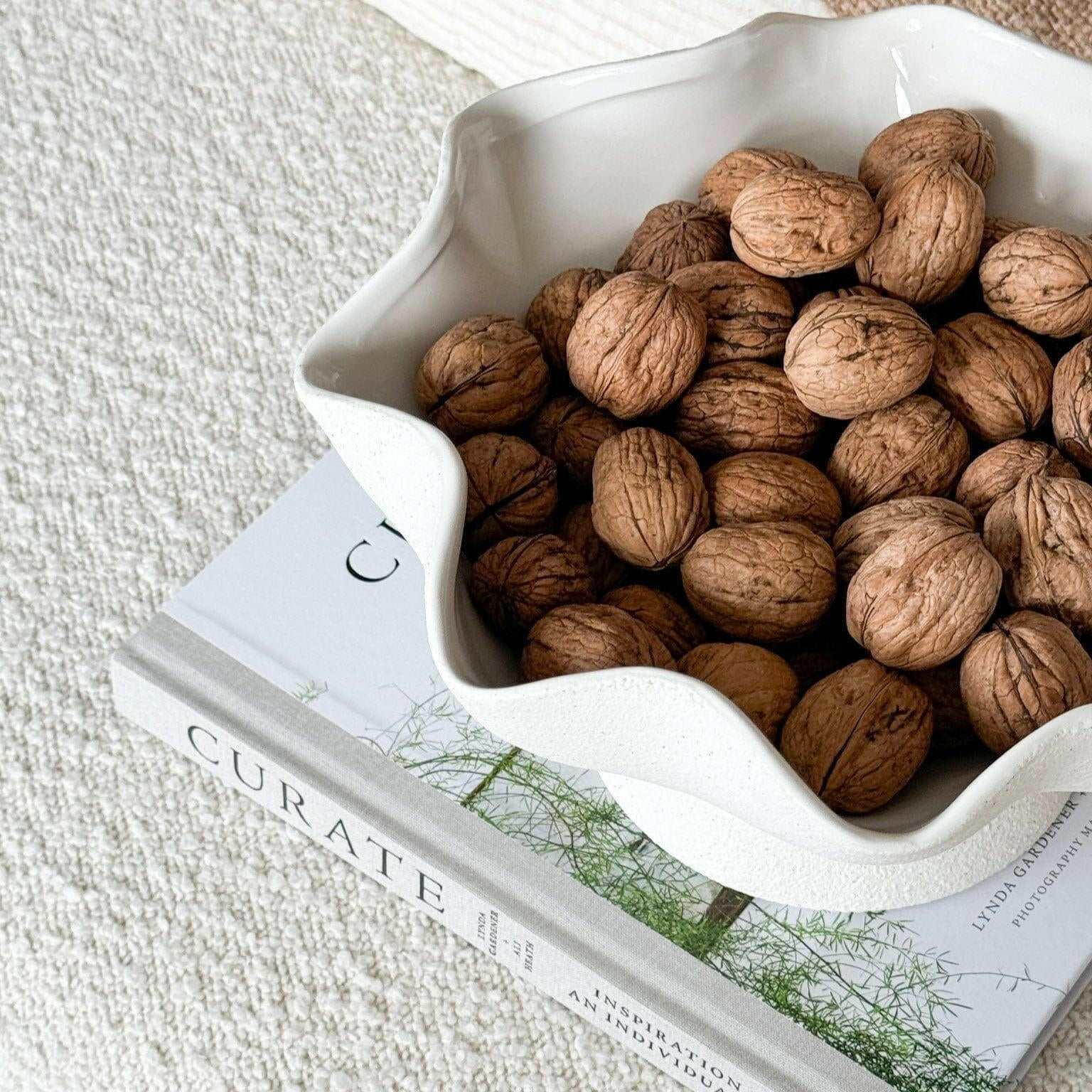 Ripple White Pedestal Bowl ceramic fruit bowl with textured exterior filled with walnuts on a book