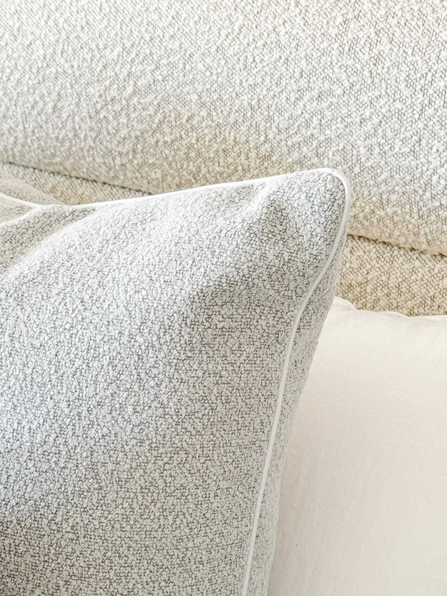 Powder blue norsu Studio Cushion in boucle fabric with white leather piping on a textured beige sofa.