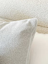 Powder blue norsu Studio Cushion in boucle fabric with white leather piping on a textured beige sofa.