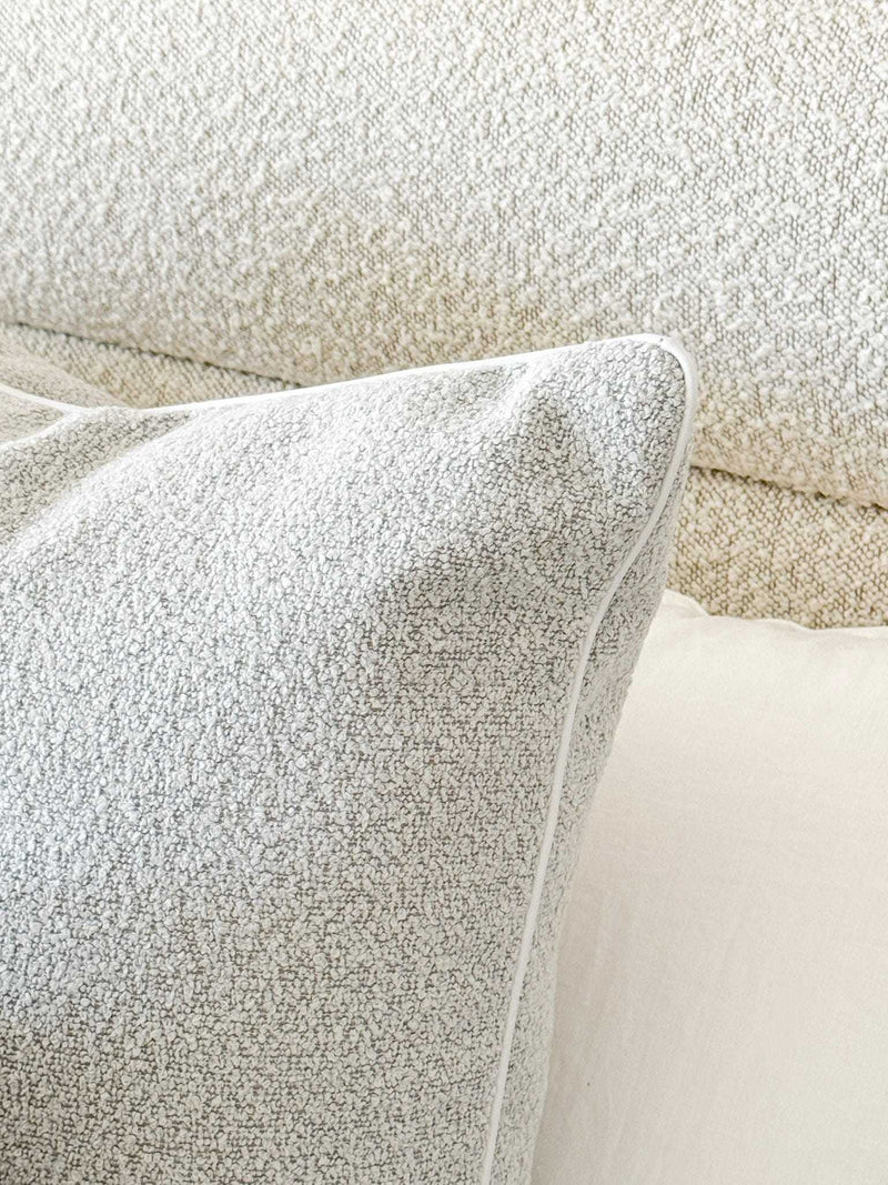 Powder blue norsu Studio Cushion in boucle fabric with white leather piping on a textured beige sofa.