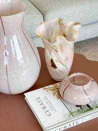 GlobeWest Boden Wave Vase Dawn handcrafted glass vase with wave design in soft dawn color on table next to pink vases and books