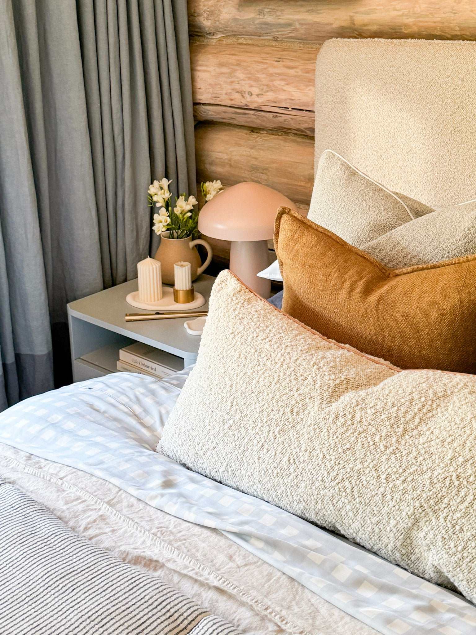 Baya Flaxmill Cushion in fenugreek color on bed with neutral bedding and wooden wall background