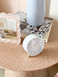 White Maisie Silent Tick Alarm Clock with gold accents and vintage design on round table