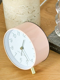 Maisie Silent Tick Alarm Clock in blush with gold legs and hands, vintage-inspired design, round shape, glass lens on wooden surface