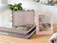 norsu Studio Scalloped Magnetic Photo Frame with scalloped edges, sage background, and clear acrylic finish displayed on books in a cozy home setting