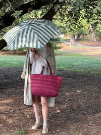 Burgundy Base Supply Take It Base Tote Bag with padded fabric and cotton straps carried outdoors under an umbrella
