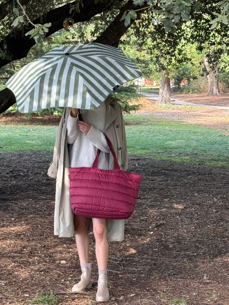Burgundy Base Supply Take It Base Tote Bag with padded fabric and cotton straps carried outdoors under an umbrella