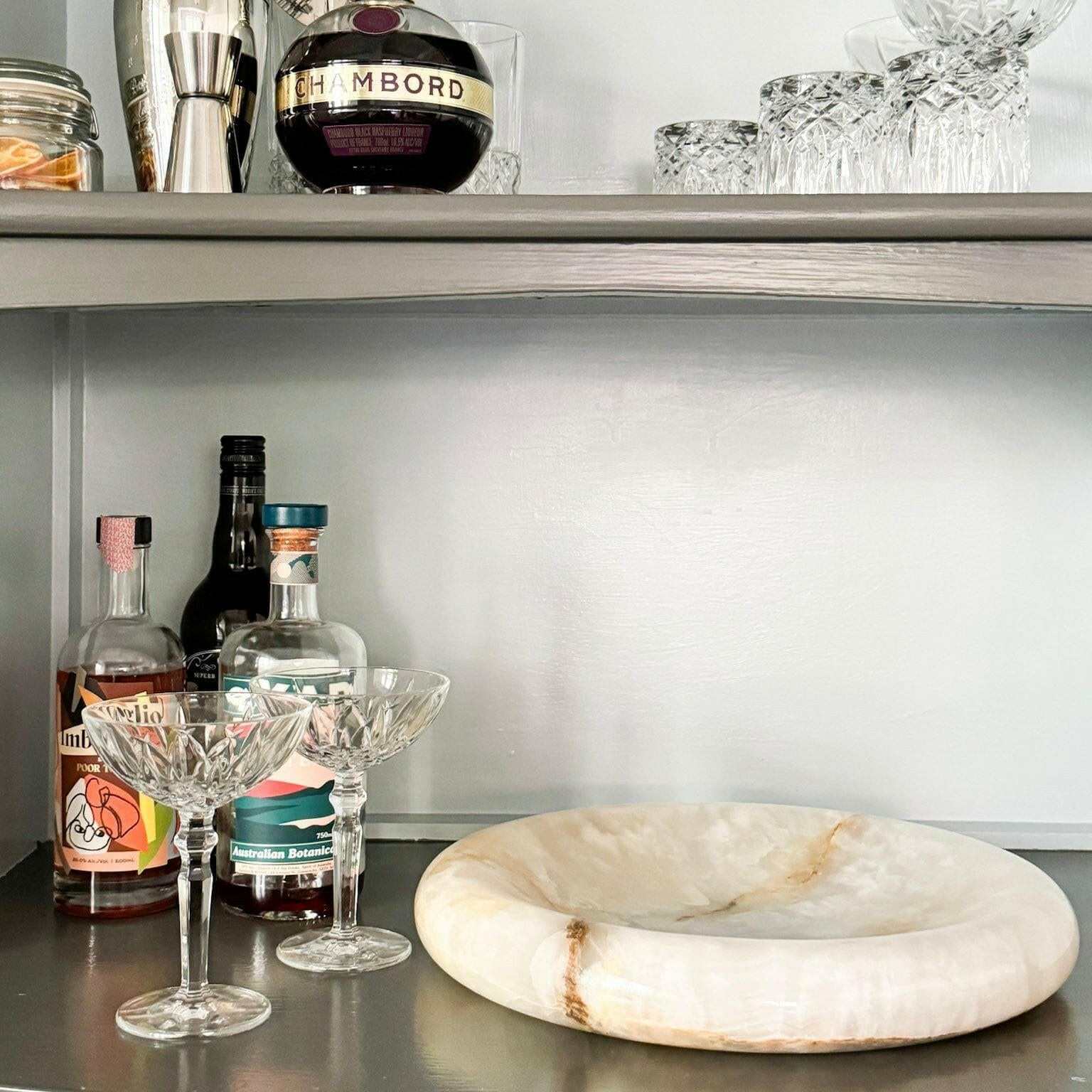 Large white onyx sculpted tray with graceful curves, placed on a countertop next to crystal glasses and bottles, showcasing elegant home decor by CoTheory Onyx Tray