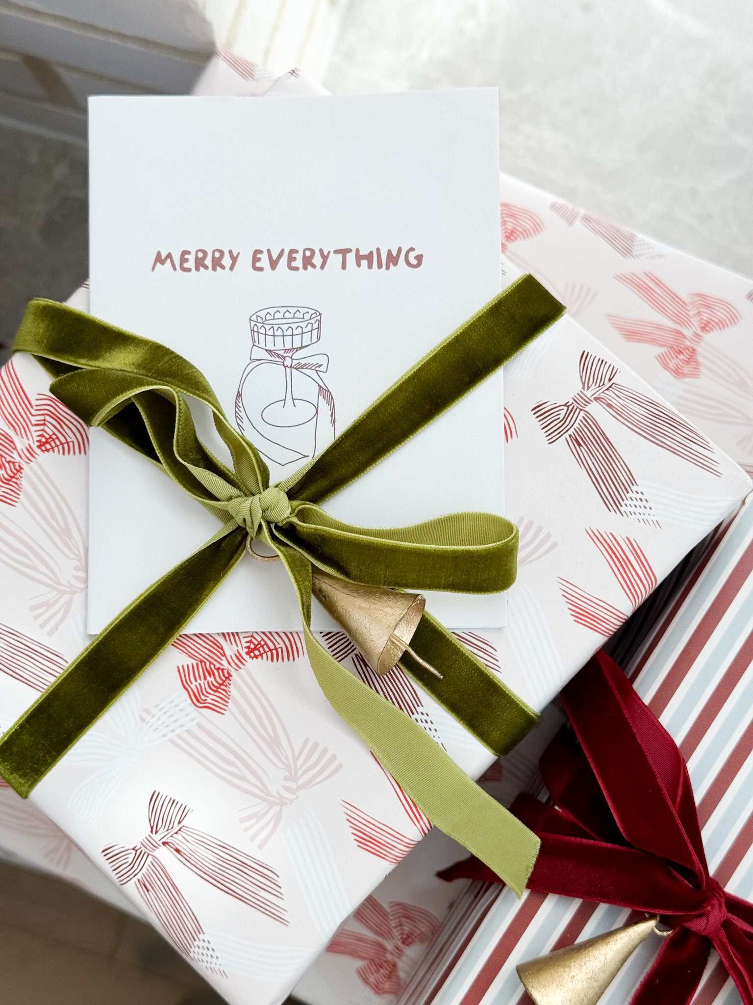 norsu STUDIO Christmas card with "Merry Everything" message and festive gift wrapping featuring green velvet ribbon and bell