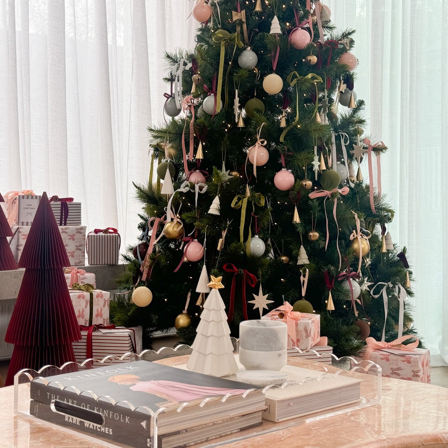 Decorated Christmas tree with ornaments and presents in a room with white curtains.