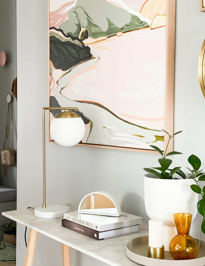 Mid-century modern Remi Desk Lamp with antique brass finish, white marble base, and frosted glass shade on a marble table.