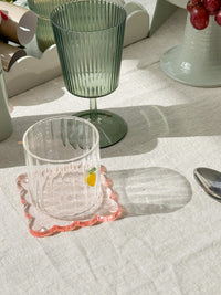 Green ribbed Saltara RPET tumbler and clear glass tumbler on white tablecloth with pink coaster and grapes nearby