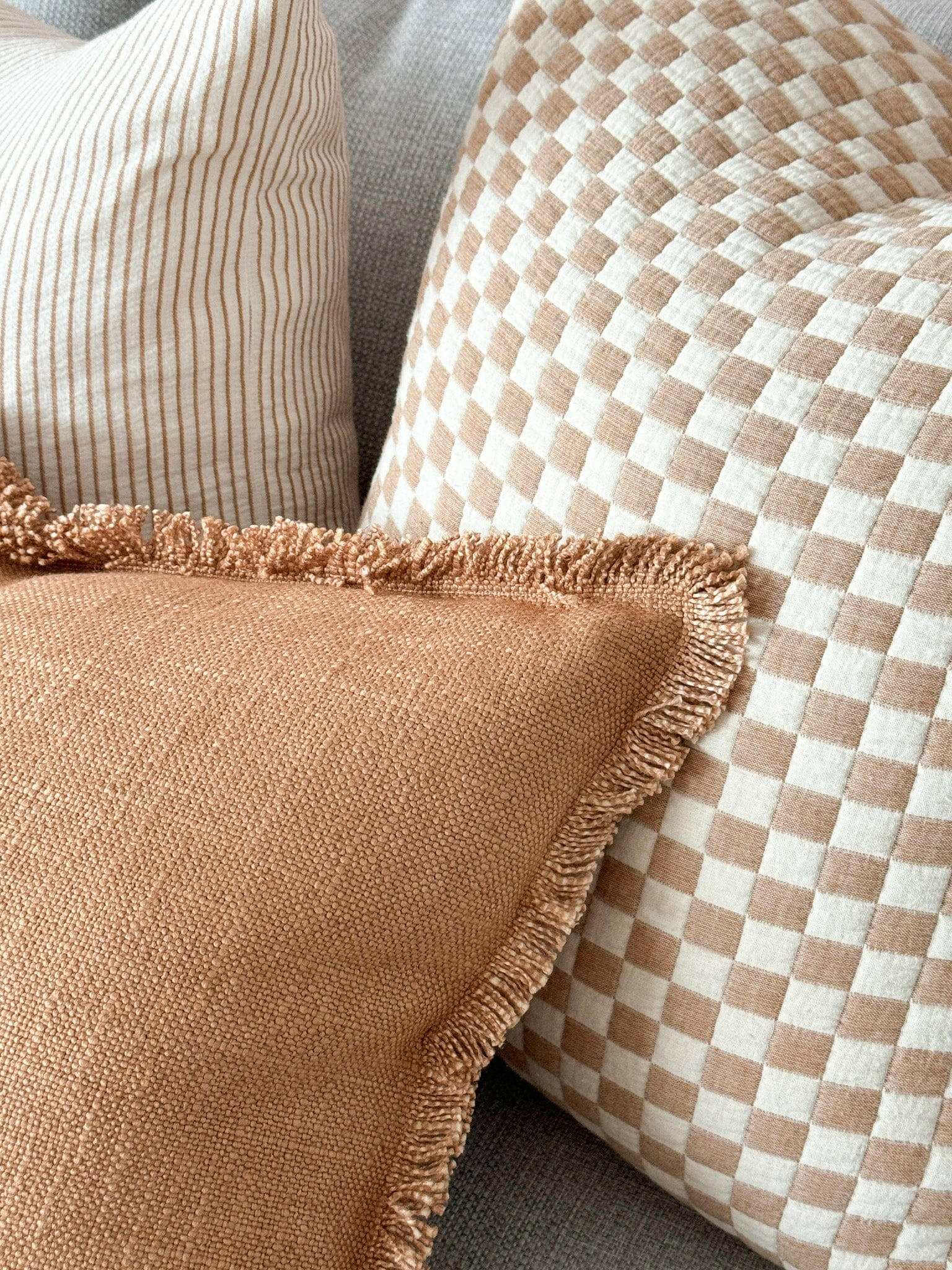 Baya Dover Cushion in nude with fringed edges and textured weave on a sofa