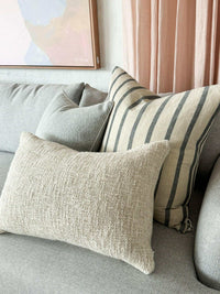 Baya Cyprian Oblong Cushion in warm oatmeal on a grey sofa with textured cotton and linen blend fabric