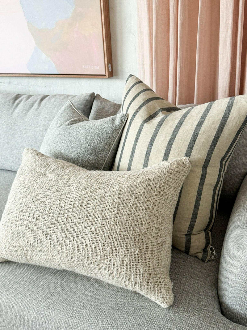Baya Cyprian Oblong Cushion in warm oatmeal on a grey sofa with textured cotton and linen blend fabric