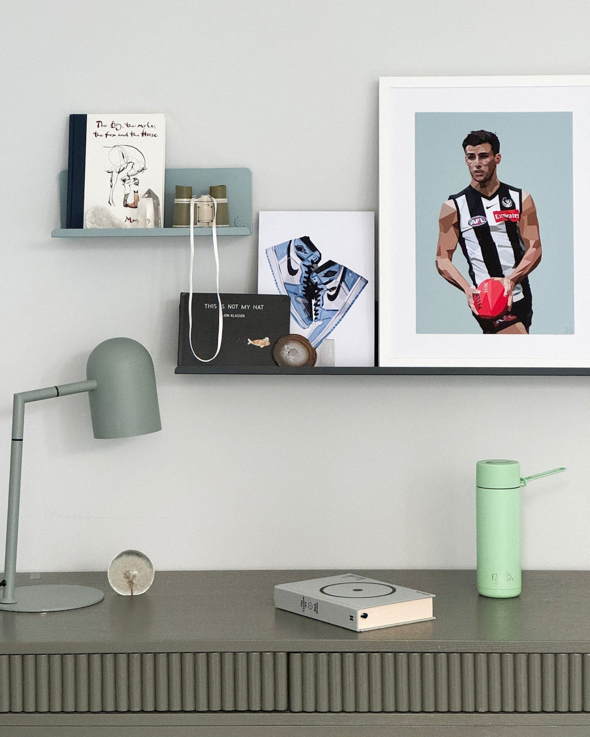 Desk setup with a lamp, books, a water bottle, and a framed picture of a person on a wall.