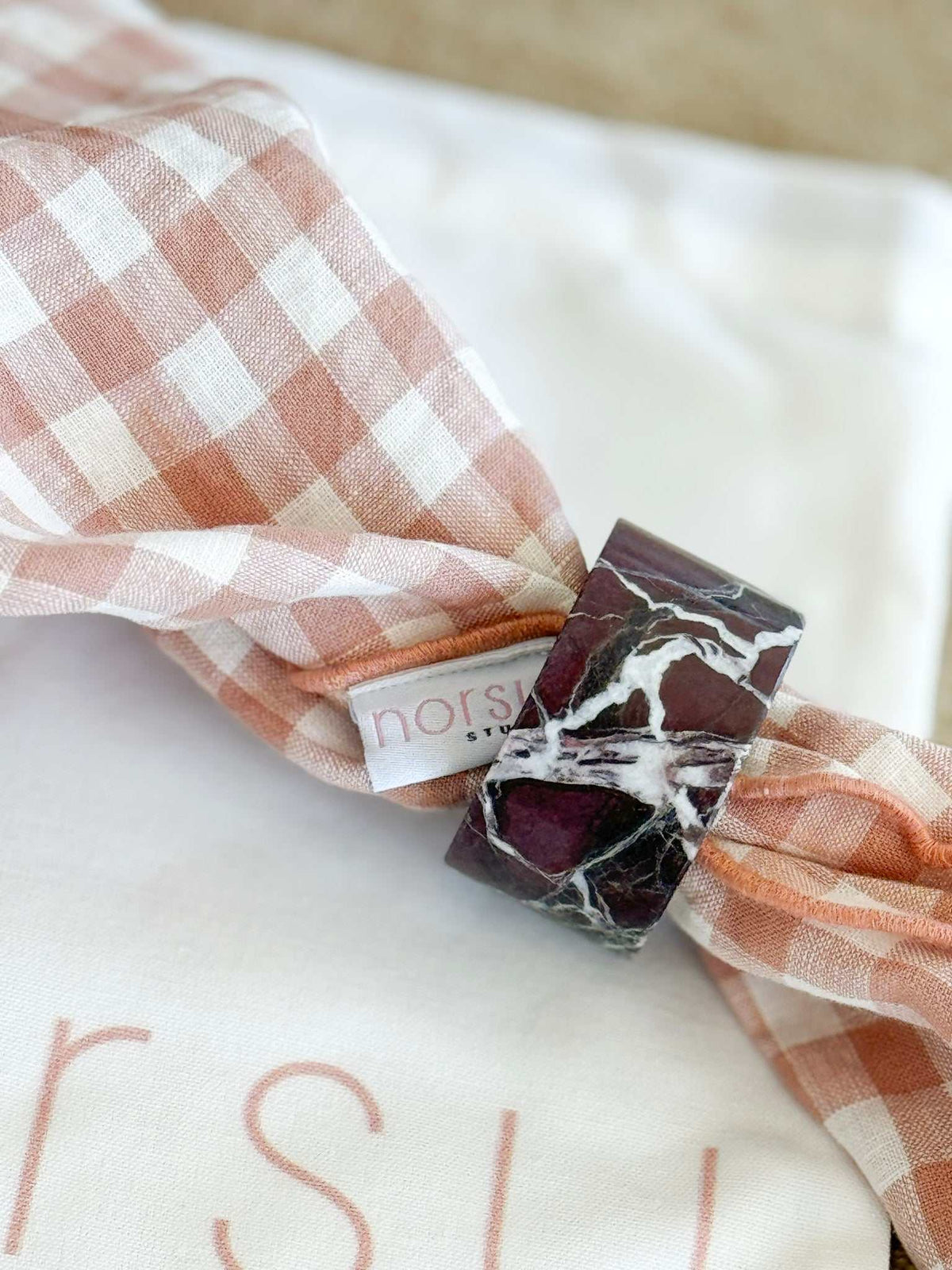 norsu STUDIO Marble Circular Napkin Ring in Rosso Levanto with deep burgundy and white veining on a pink checkered napkin