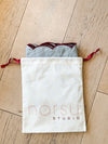 norsu Studio Linen scallop-edged blue napkins with deep burgundy edge in drawstring storage bag on wooden floor