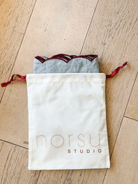 norsu Studio Linen scallop-edged blue napkins with deep burgundy edge in drawstring storage bag on wooden floor