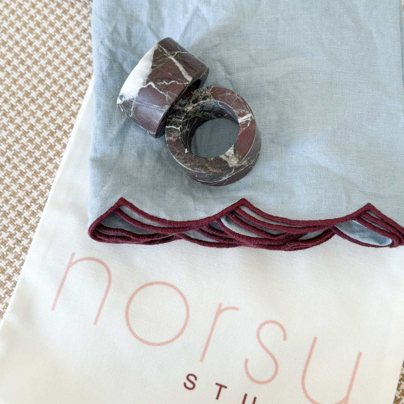 norsu Studio Linen scallop-edged blue napkin with deep burgundy trim and marble napkin rings on linen cloth
