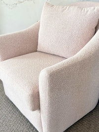 Blush boucle norsu Studio Swivel Chair with feather cushion and curved armrests in a cozy bedroom setting