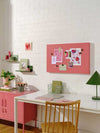 Berry color Story Board with magnetic surface mounted on white brick wall above a white desk in a pink and green themed room