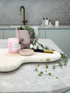 Stylish kitchen bench vignette with pink candle, plant in pot, textured cutting board, and modern brass faucet
