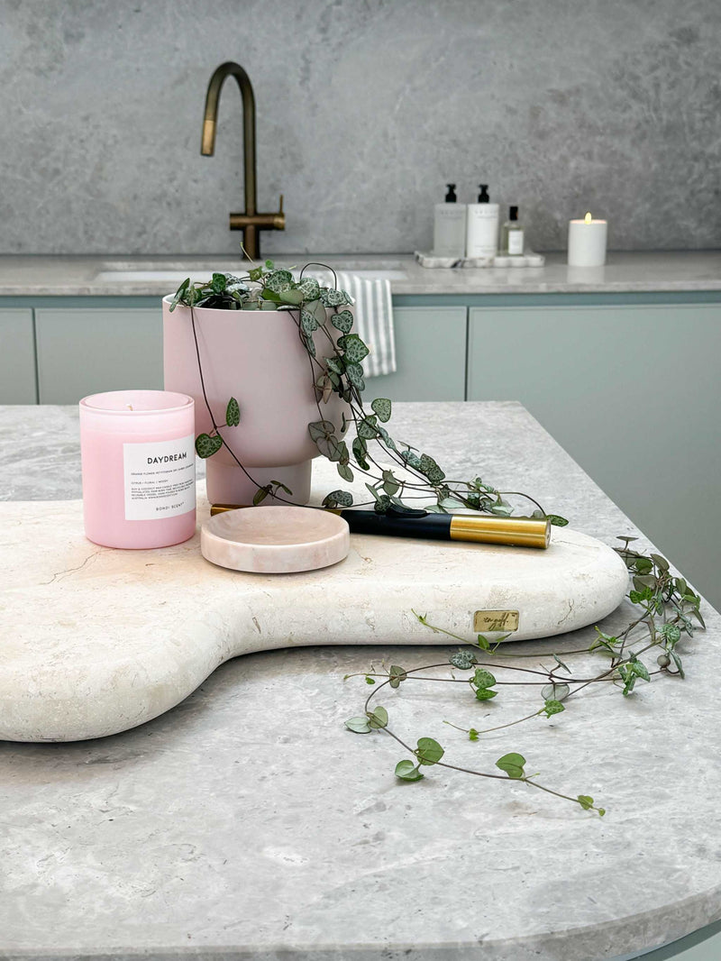 Stylish kitchen bench vignette with pink candle, plant in pot, textured cutting board, and modern brass faucet