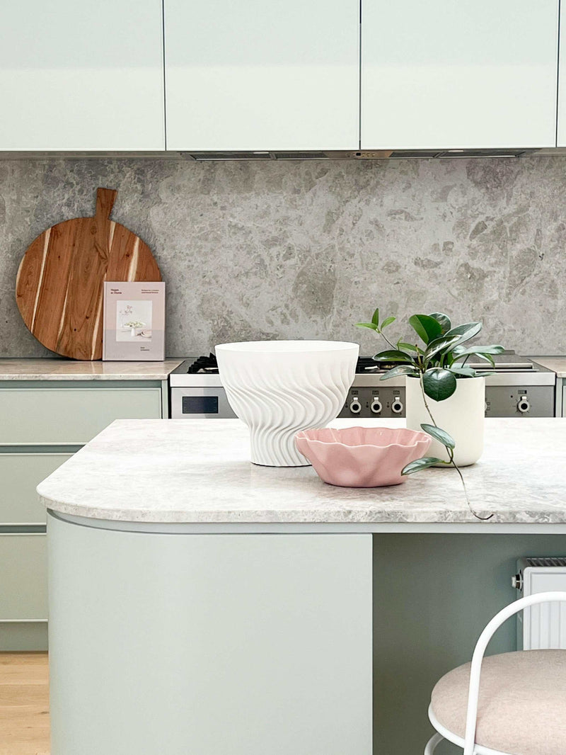 Modern styled kitchen bench with decorative bowls, potted plant, and wooden cutting board against a marble backsplash