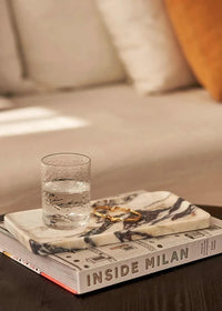 Linea Rectangle Marble Tray in Calacatta Viola with violet veins, styled with a glass of water and a gold bracelet on a book.