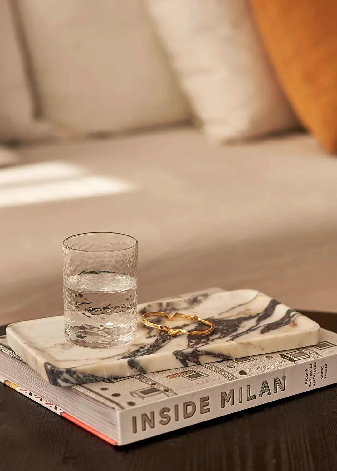 Linea Rectangle Marble Tray in Calacatta Viola with violet veins, styled with a glass of water and a gold bracelet on a book.