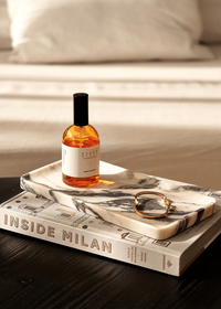 Linea Rectangle Marble Tray in Calacatta Viola marble with violet veins, holding perfume and jewelry on a book.