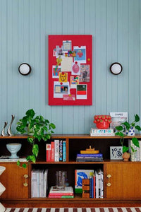 Red magnetic storyboard with photos and notes, mounted above a wooden cabinet with books and plants, designed to complement Mustard Made lockers.