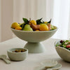 Aries resin pedestal bowl in sage green filled with fruit on a dining table centerpiece