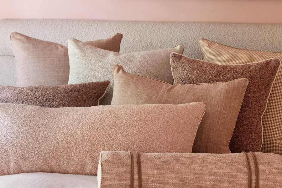 A layered stack of norsu cushions in blush, clay and boucle on a bed
