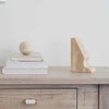 Beige travertine Orbit Sphere Table Sculpture on stacked books beside a beige travertine bookend on wooden surface
