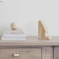 Beige travertine Orbit Sphere Table Sculpture on stacked books beside a beige travertine bookend on wooden surface