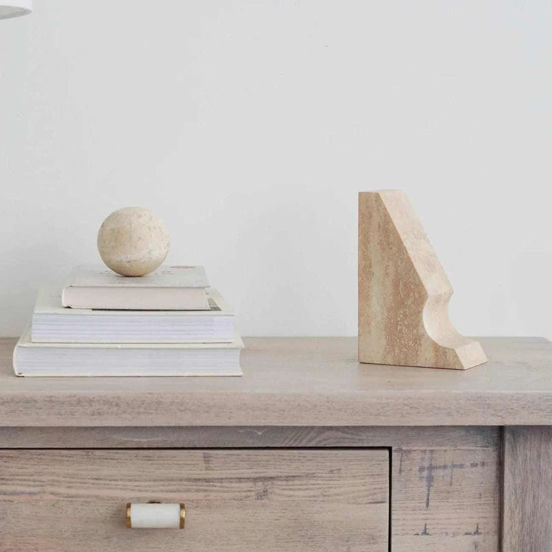 Beige travertine Orbit Sphere Table Sculpture on stacked books beside a beige travertine bookend on wooden surface
